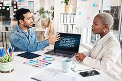 Website designer LBI meeting with a client over a laptop that reads SEO Services on the screen