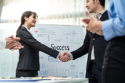 NCR dealer shaking hands with branch manager in front of white board that says "SUCCESS"