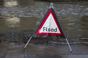 Red and white flood warning sign standing in floodwater on a road, a reminder to check flood risk when buying Seaside Park real estate